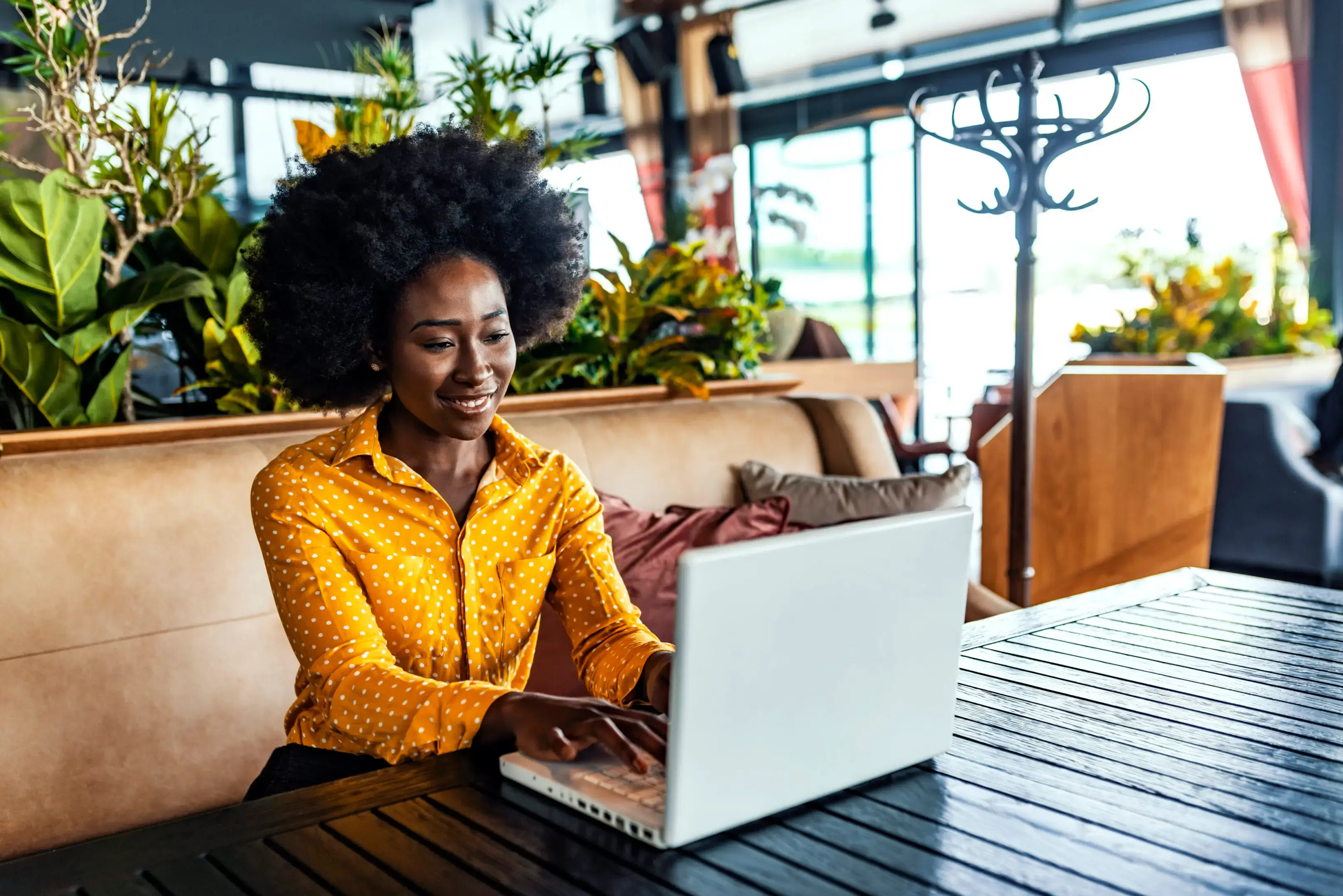 Woman using laptop at plant-filled cafe